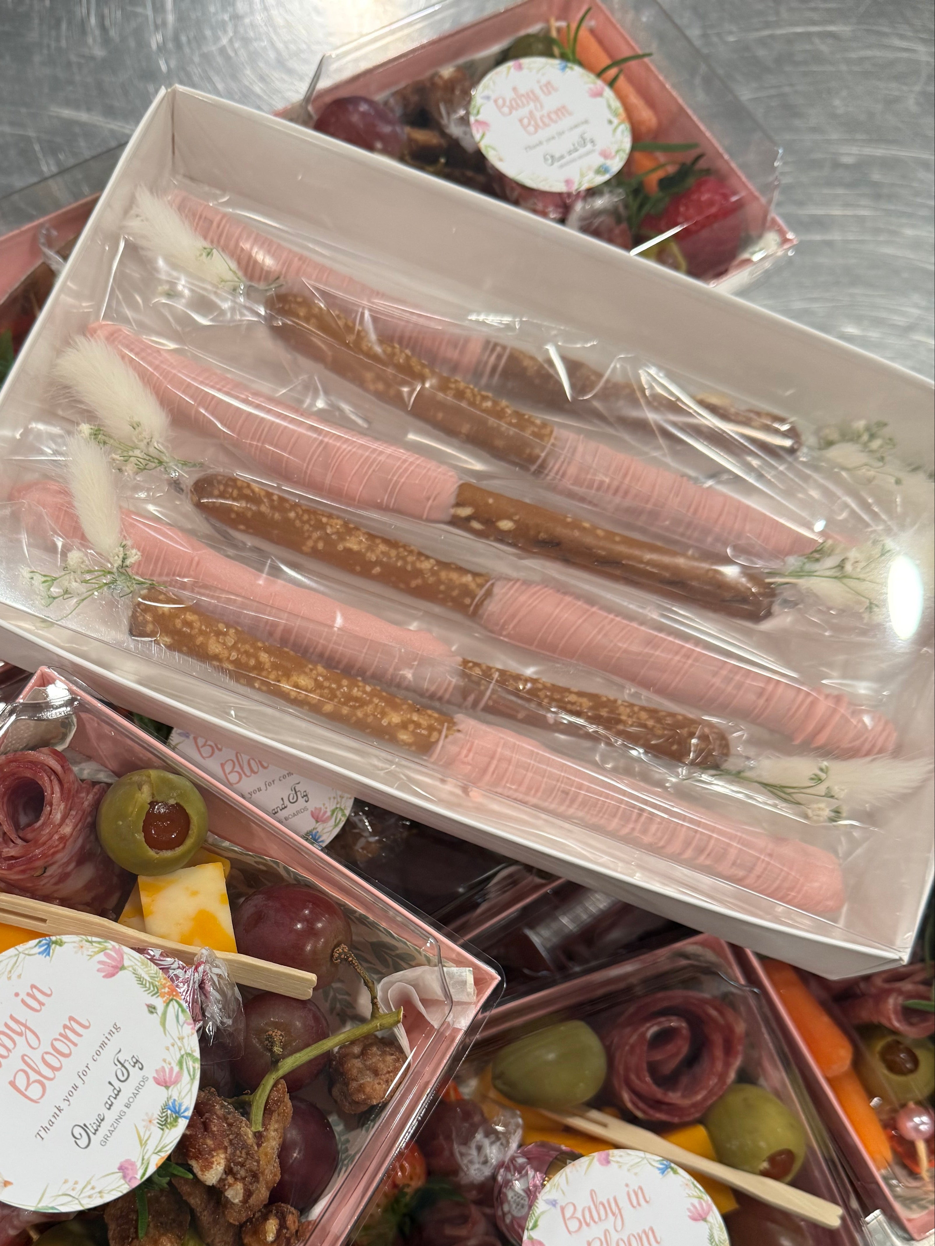 Assorted snacks in clear containers with decorative labels on a metal surface.