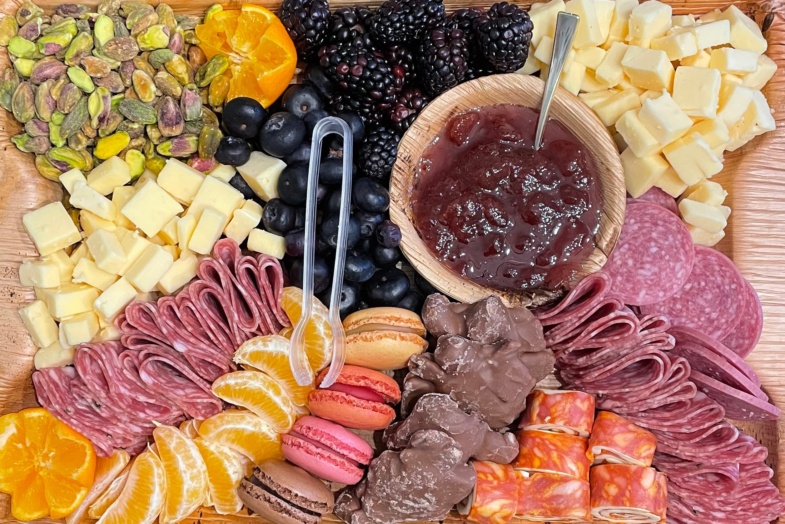 Wooden charcuterie board with assorted meats, cheeses, fruits, and nuts on a wooden surface.