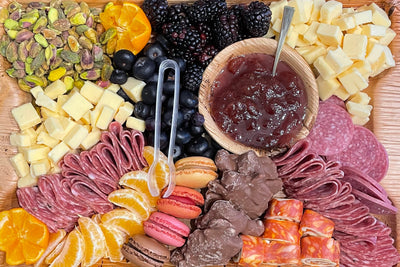 Wooden charcuterie board with assorted meats, cheeses, fruits, and nuts on a wooden surface.