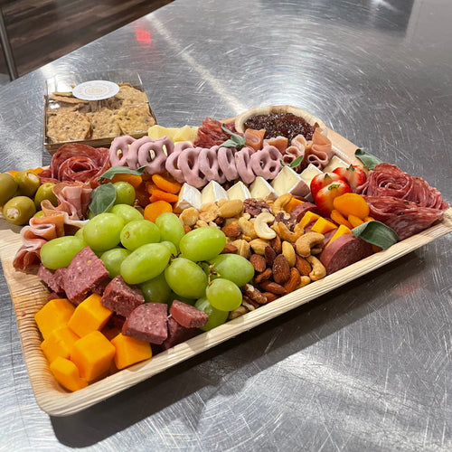 Assorted deli meats and cheeses in a wooden tray on a metal surface.