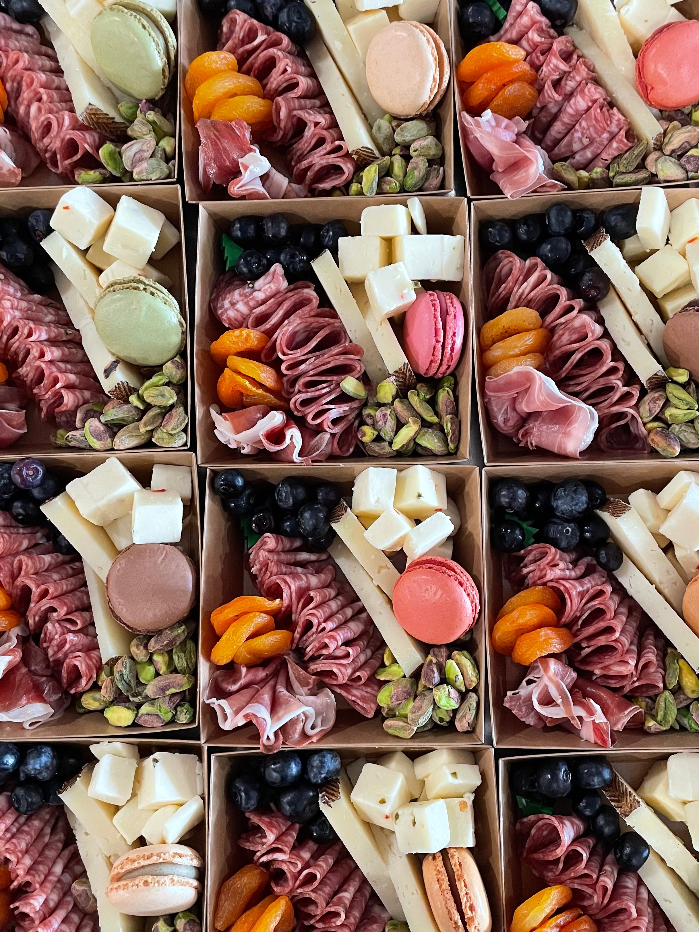 Assorted pastries and fruits in small boxes arranged in a grid.
